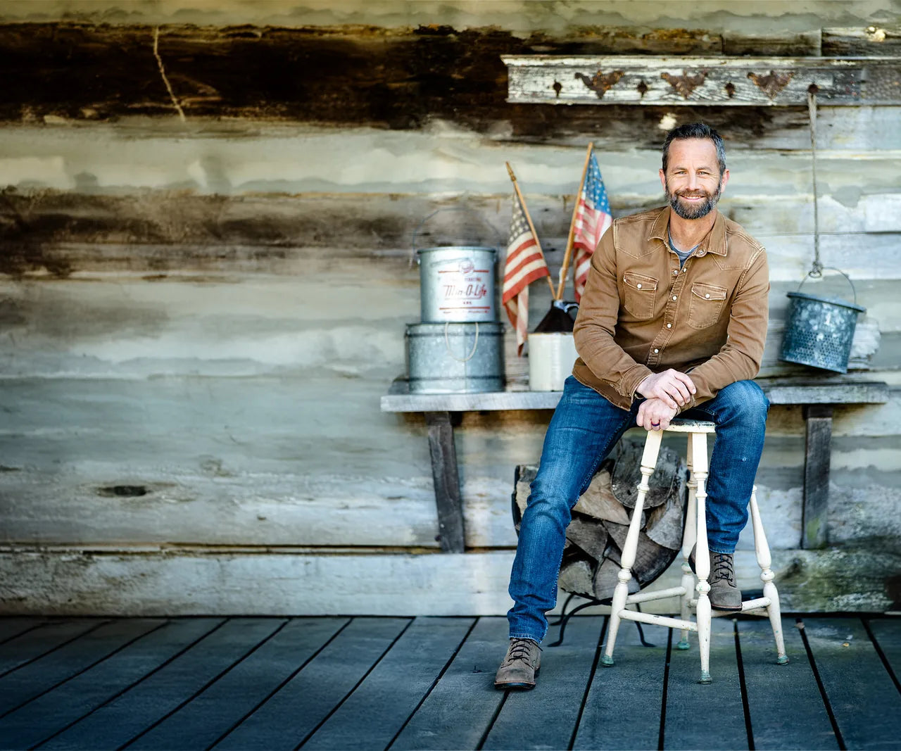 Kirk Cameron seated on a stool in front of a weathered timber wall